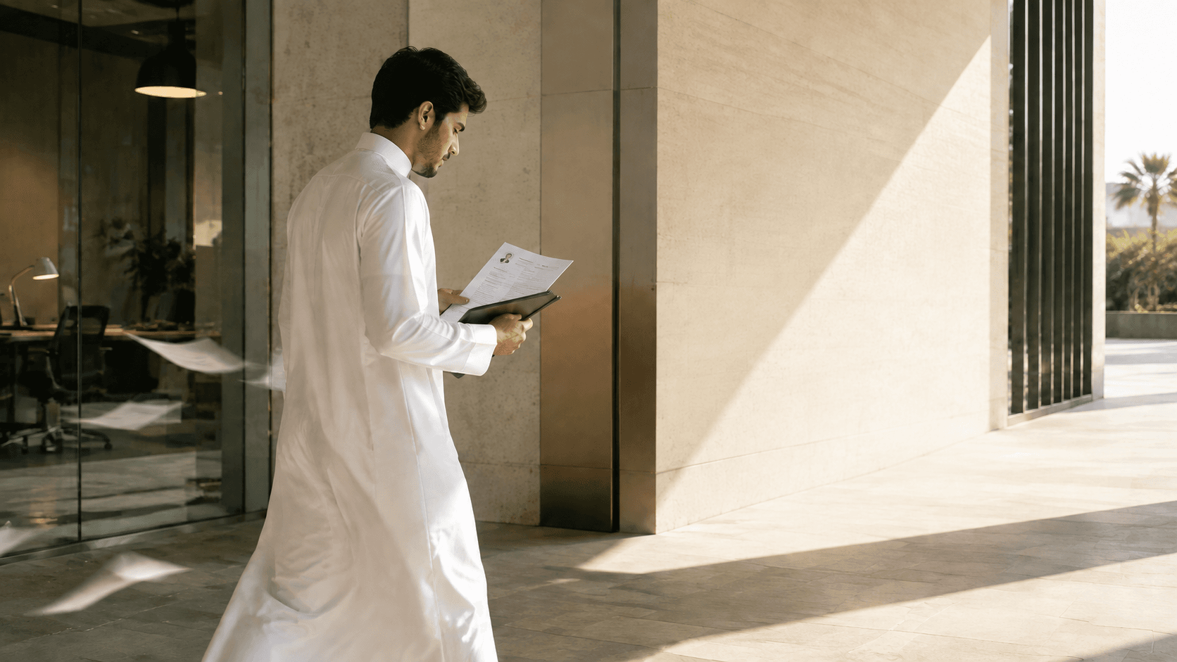 شاب سعودي يمشي في ممر مهني مضاء وهو يراجع سيرته الذاتية